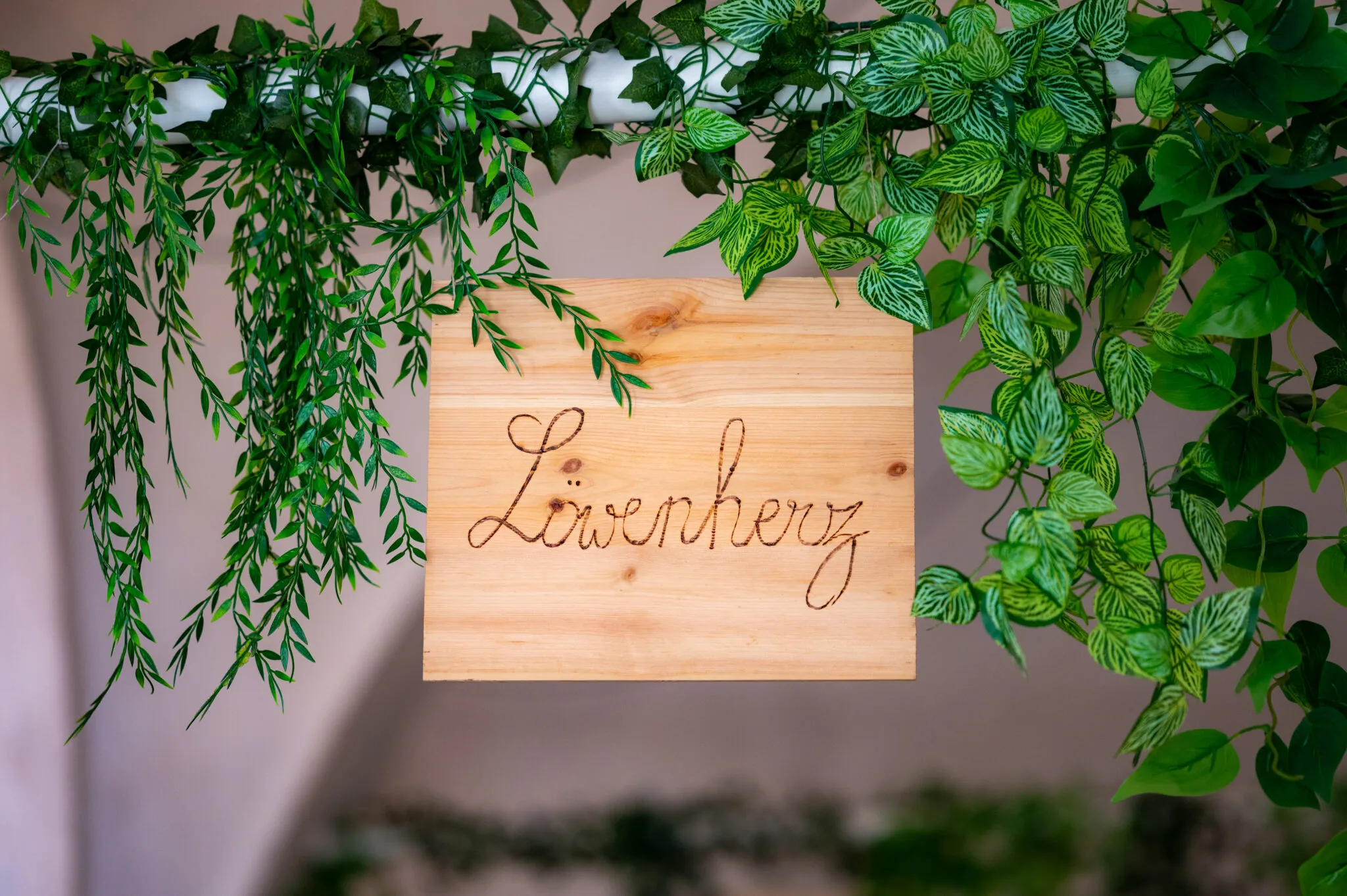 Holzschild mit dem Schriftzug Löwenherz zwischen hängenden Pflanzen
